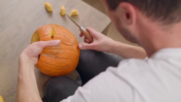 Young man carves teeth in Jack Lantern with a knife — ストック動画