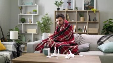 Üşümüş bir adam oturma odasındaki kanepede kendini battaniyeye sarar.