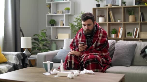 Ill hombre utiliza un teléfono inteligente en casa en el sofá — Vídeo de stock