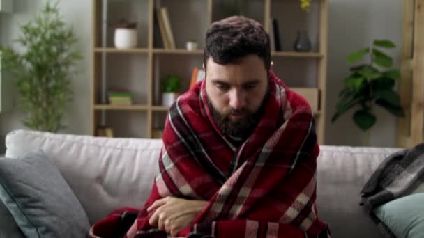 Nemocný muž s zimnicí a zabalí se do deky na pohovce v obýváku — Stock video