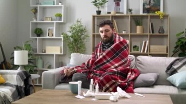 Üşümüş bir adam oturma odasındaki kanepede kendini battaniyeye sarar.