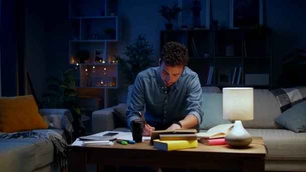 Ung man dansar medan han sitter på en soffa medan han studerar på natten — Stockvideo