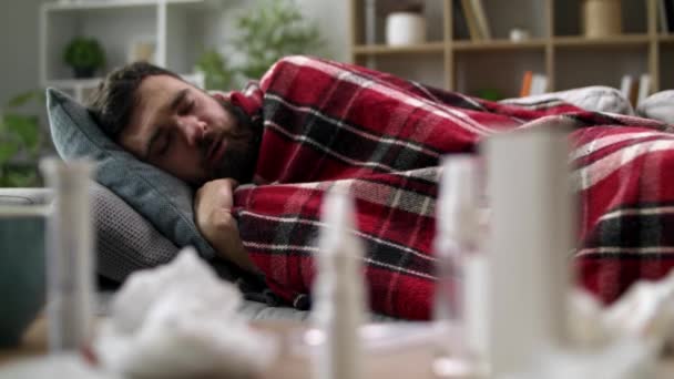 Kranker Mann mit Schüttelfrost und hüllt sich in eine Decke auf dem Sofa im Wohnzimmer — Stockvideo