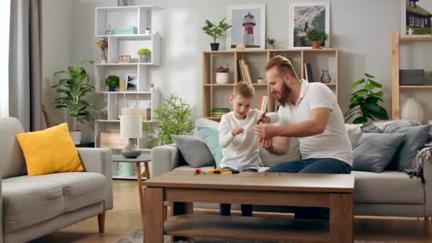 Far och son leker med en barndesigner i vardagsrummet — Stockvideo