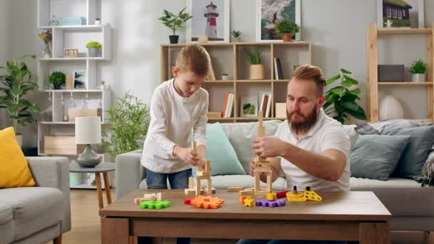 Ojciec i syn budują wieże z drewnianych klocków w salonie — Wideo stockowe