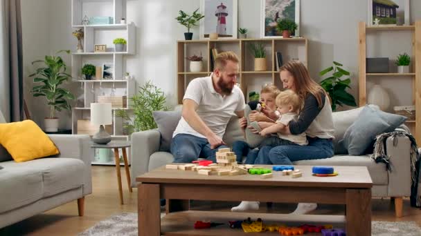 Щаслива сім'я грає з іграшковим пінгвіном, сидячи на дивані у вітальні — стокове відео