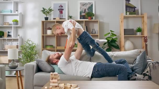Otec vychovává svého syna na gauči. Syn skočí na otce.. — Stock video