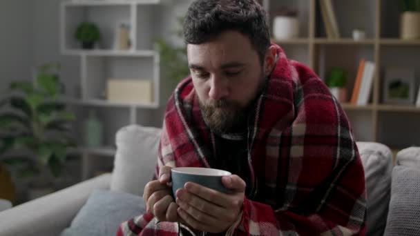 Cold man drinks tea on the sofa in the living room — Stock Video