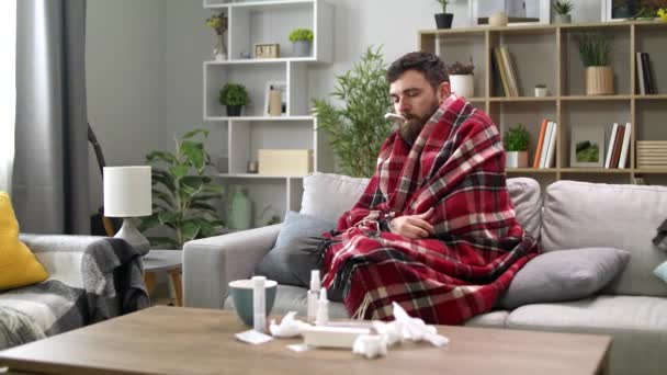 Ein kranker Mann misst die Temperatur zu Hause auf dem Sofa — Stockvideo