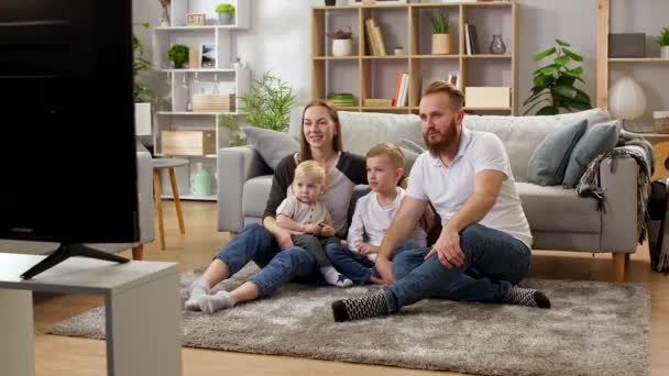 Familia viendo la televisión mientras está sentado en el piso de la sala de estar — Vídeos de Stock