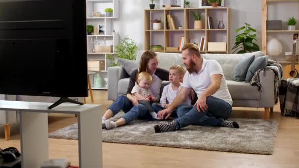 Семья смотрит телевизор, сидя на полу гостиной — стоковое видео