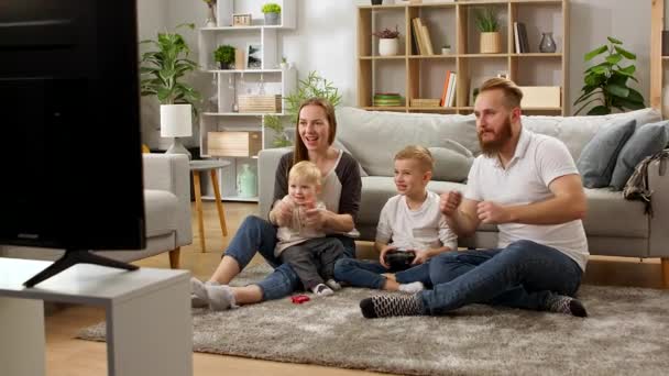 Un chico con un mando juega videojuegos con papá, mamá y hermanito — Vídeos de Stock