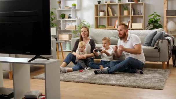 Un chico con un mando juega videojuegos con papá, mamá y hermanito — Vídeos de Stock