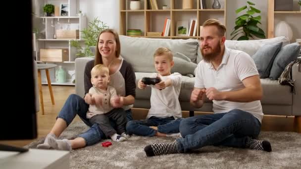 En pojke med en gamepad spelar tv-spel med pappa, mamma och lillebror — Stockvideo