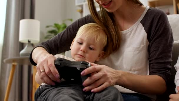 Bambino con un gamepad seduto sulle ginocchia di sua madre — Video Stock