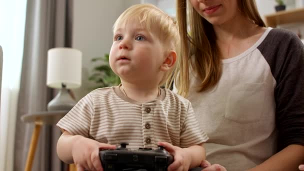 Pojke med en gamepad sittande i sin mors knä — Stockvideo