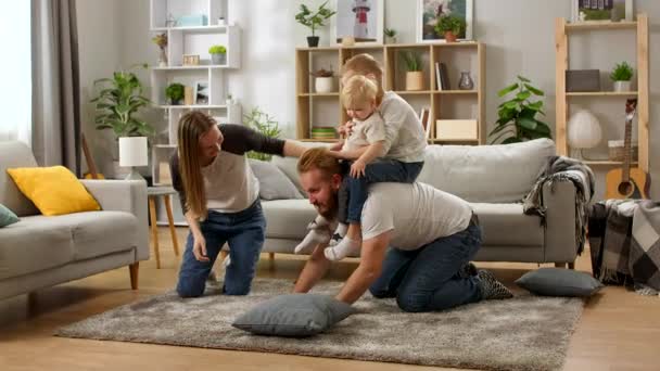 Joven papá arrastrándose en el suelo llevando lindo niño pequeño hijos en la espalda — Vídeo de stock