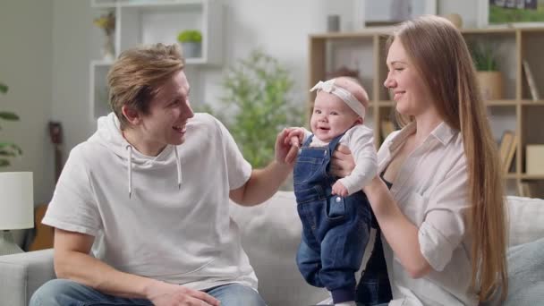 Lycklig mor och far med bebis dotter sitter på soffan hemma — Stockvideo