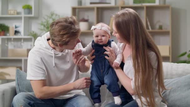 幸せな母親と父親と赤ちゃんの娘は家でソファに座って — ストック動画