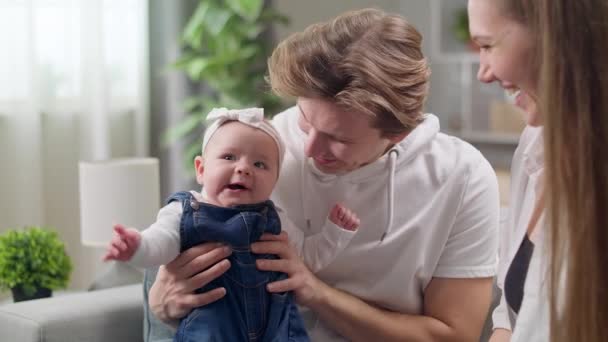 Feliz madre y padre con hija bebé sentado en el sofá en casa — Vídeos de Stock