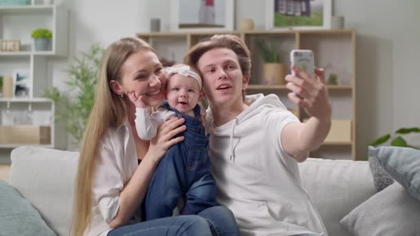 Jovem família tirando uma selfie no sofá na sala de estar — Vídeo de Stock