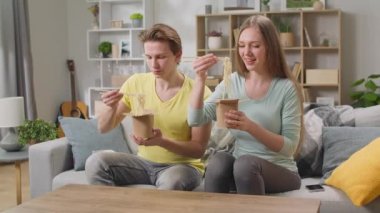 Evde yemek çubuklarıyla kutudan erişte yiyen genç bir çift.