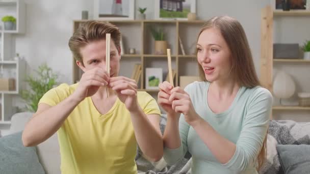 Pareja joven preparando palillos en casa en la sala de estar — Vídeos de Stock