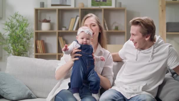 Feliz madre y padre con hija bebé sentado en el sofá en casa — Vídeo de stock