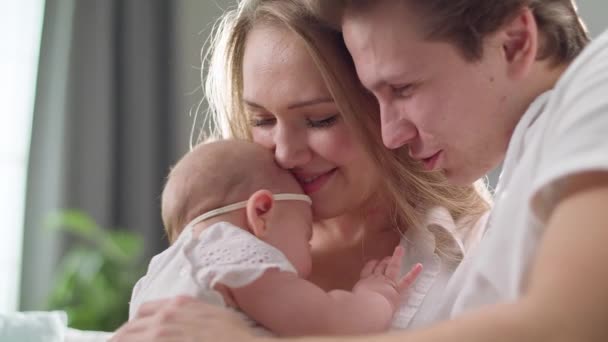 Mom and dad kisses and hugs a little daughter in the morning sun — 비디오