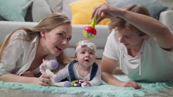Маленькая девочка играет погремушку с родителями — стоковое видео