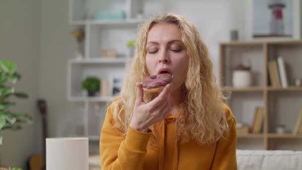 Vrolijk meisje eet smakelijk donut thuis op de bank — Stockvideo