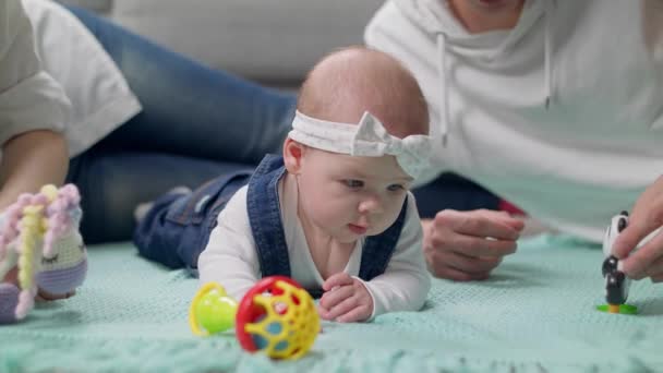 Meisje kind speelt een rammelaar op de vloer met ouders — Stockvideo