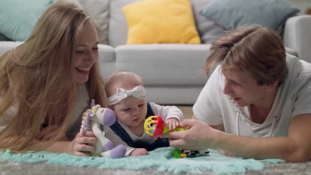 Meisje kind speelt een rammelaar op de vloer met ouders — Stockvideo