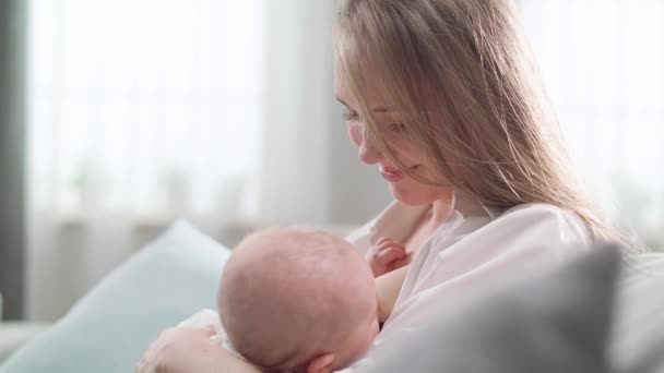 Mam geeft borstvoeding aan haar dochtertje in de ochtendzon in de woonkamer — Stockvideo