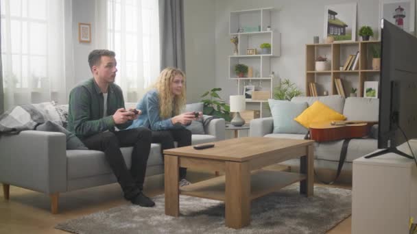 Joven hombre y mujer juegan juntos en una consola en casa — Vídeos de Stock