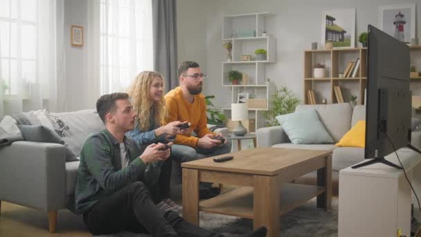A barátok videojátékoznak, miközben egy kanapén ülnek a nappaliban. — Stock videók