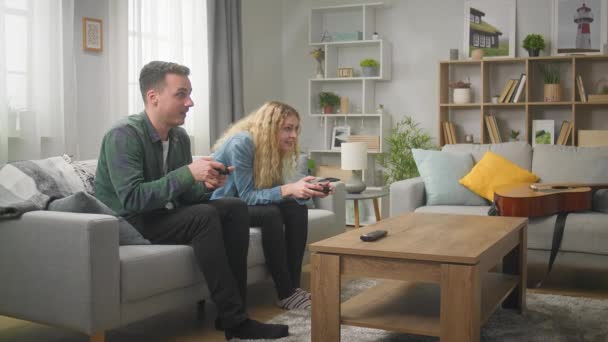 Joven hombre y mujer se divierten con gamepads en la sala de estar — Vídeos de Stock