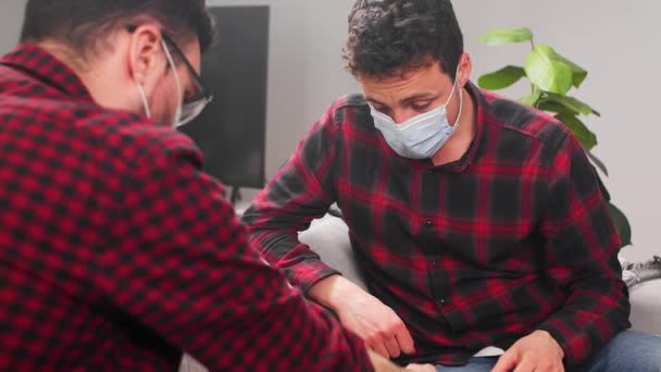 Dos jóvenes con máscaras médicas juegan al ajedrez en casa en cuarentena. . — Vídeos de Stock