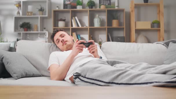 Un hombre sin entusiasmo en casa en el sofá y juega videojuegos — Vídeo de stock