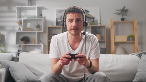 Un giovane uomo gioca online videogiochi con le cuffie su un divano durante la quarantena — Video Stock