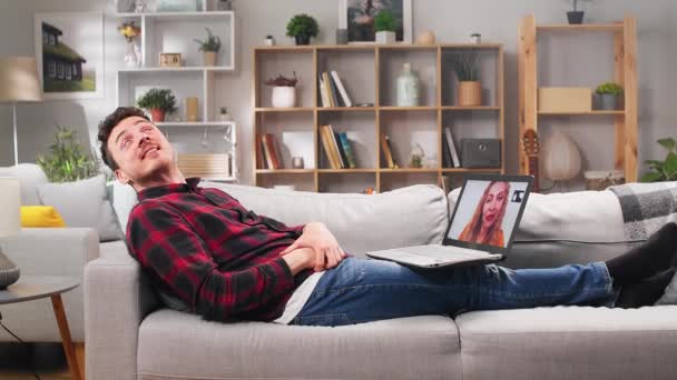 El hombre se comunica con una chica a través de videollamadas a través de un ordenador portátil en su sala de estar — Vídeos de Stock
