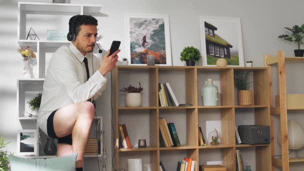 Młody człowiek prowadzi wideokonferencję za pomocą smartfona podczas kwarantanny w swoim salonie — Wideo stockowe