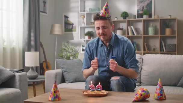 Een jonge vrolijke man doet een wens en blaast kaarsen uit. Eenzame verjaardag concept. — Stockvideo