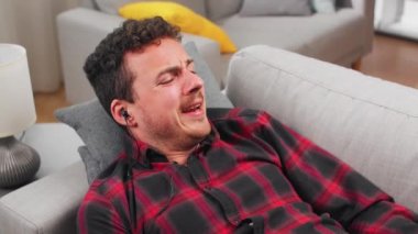 Genç bir adam kanepede yatarken müzik dinler ve kulaklıkla dans eder.
