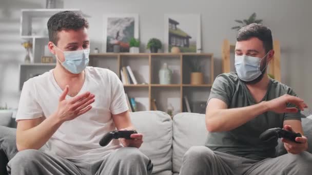 Двоє молодих чоловіків в масках грають в комп'ютерні ігри і дезінфікують руки . — стокове відео