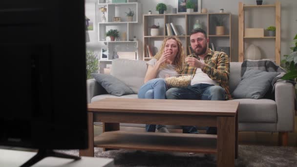 Пара дивиться телевізор, сидячи на дивані і їдячи попкорн — стокове відео