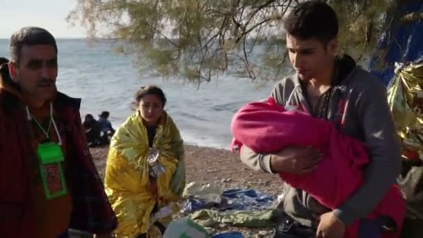 莱斯沃斯，希腊-2015 年 11 月 5 日︰ 年轻男子抱着一个婴儿在岸上. — 图库视频影像