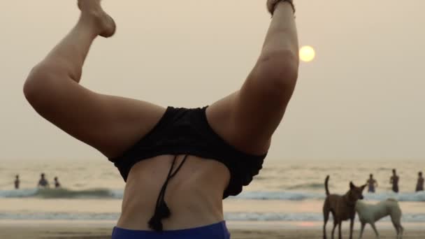 Arambol, Goa, India - 30 december 2019: Jong slank meisje in yoga poseert op een zandstrand aan zee bij zonsondergang. — Stockvideo