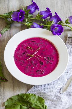 Pancar, pancar çorbası bırakır. Beyaz tabak, ahşap arka plan, çiçekler.