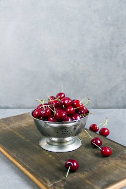 Gümüş bir kevgir/elek bir ahşap tahta üzerinde taze, tatlı kiraz. Gri arka planı.